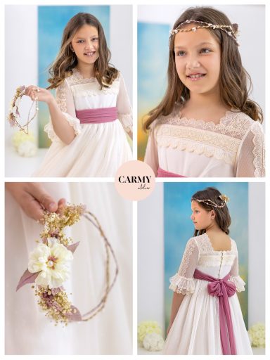 Niña sonriente en un vestido blanco con cinta rosa, sosteniendo una corona de flores.