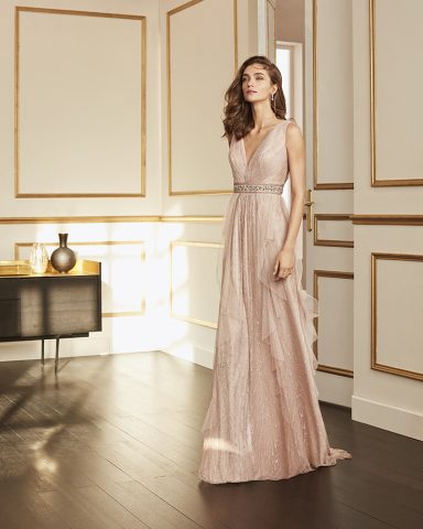 Mujer con vestido largo rosa claro en un interior elegante con decoración clásica.