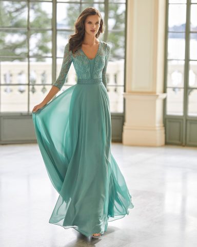 Mujer en vestido largo verde claro, sonriendo en un ambiente luminoso y elegante.