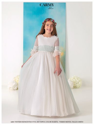 Niña sonriente en un vestido blanco con cintilla azul, fondo azul claro.