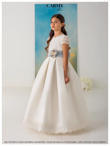 Niña con vestido blanco largo y cinturón plateado, posando con fondo suave.