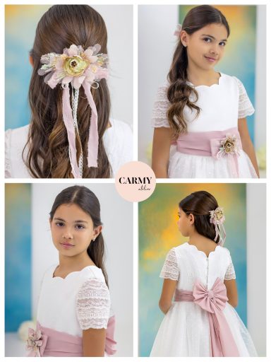 Niña con vestido blanco y cinta rosa, adornos florales en el cabello.