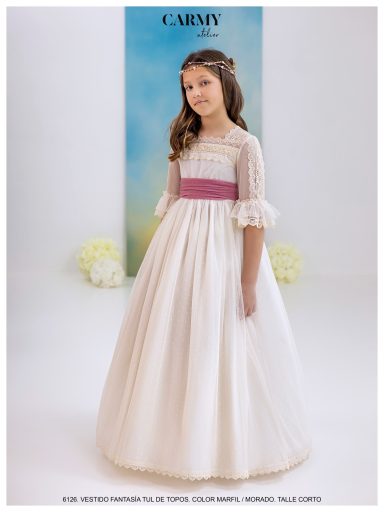 Niña con vestido blanco y cintilla rosa, sonriente, de pie en un fondo azul.