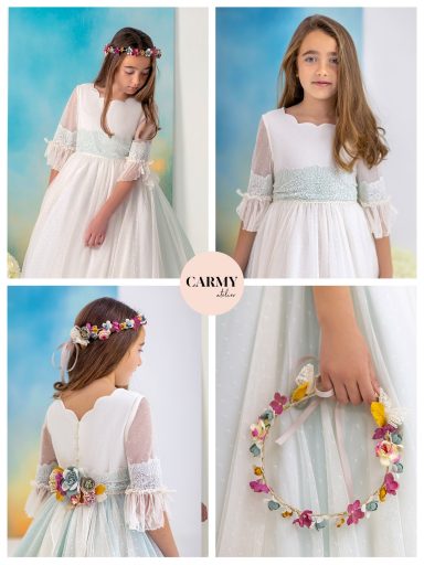 Niña con vestido blanco y lazo celeste, sosteniendo una corona de flores. Fondo colorido.