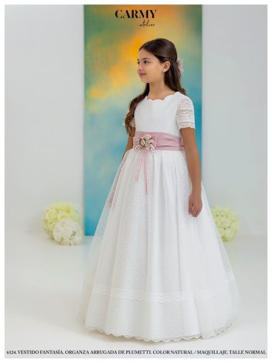 Niña con vestido blanco y cinta rosa, de pie en una pose elegante, fondo azul.