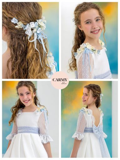 Niña sonriente con pelo ondulado, vestido blanco y adornos florales en el cabello.