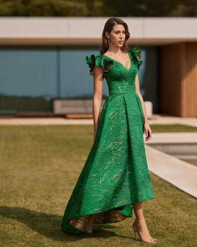 Mujer en vestido verde elegante con mangas rizadas, de pie en un jardín moderno.