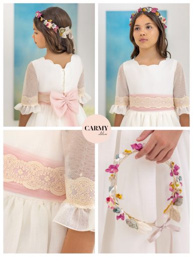 Niña con vestido blanco, lazo rosa y diadema de flores, sonriente en fondo suave.