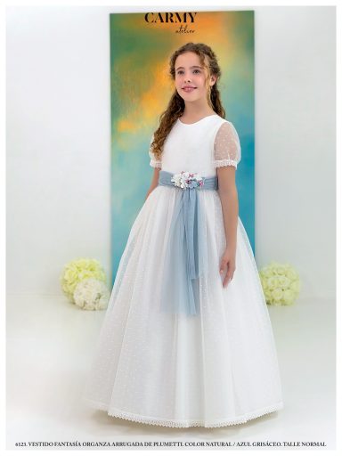 Niña con vestido blanco y cinta azul, sonriendo frente a un fondo colorido.