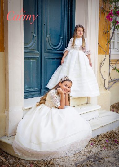 Dos niñas en vestidos de fiesta blancos, una sentada y otra de pie en una escalera.