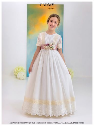 Niña sonriendo con vestido blanco largo, decorado con flores en la cintura. Fondo resplandeciente.